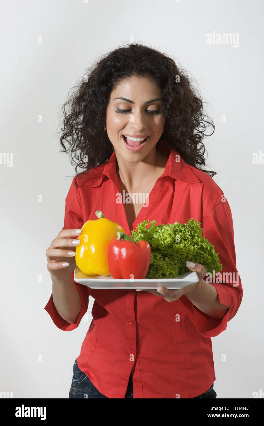 Femme tenant une assiette de légumes crus et souriant Banque D'Images