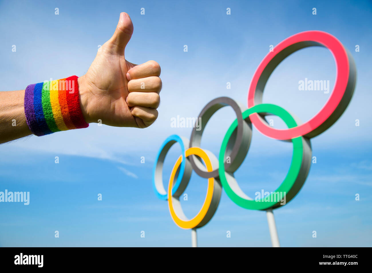 Londres - 4 mai 2019 : une main portant des gay pride rainbow bracelet de couleur donne un geste thumbs-up en face d'Anneaux olympiques en bleu ciel. Banque D'Images