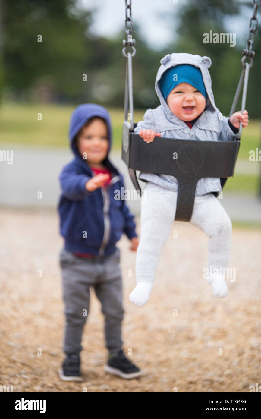 Petit garçon poussant baby sister on swing Banque D'Images