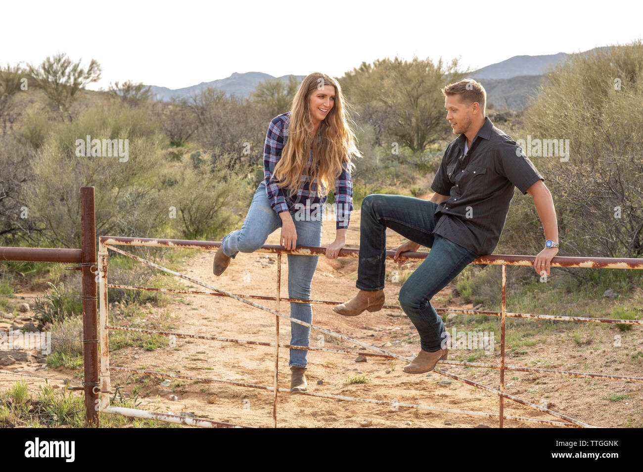 Western wear young couple sitting on ranch gate Banque D'Images