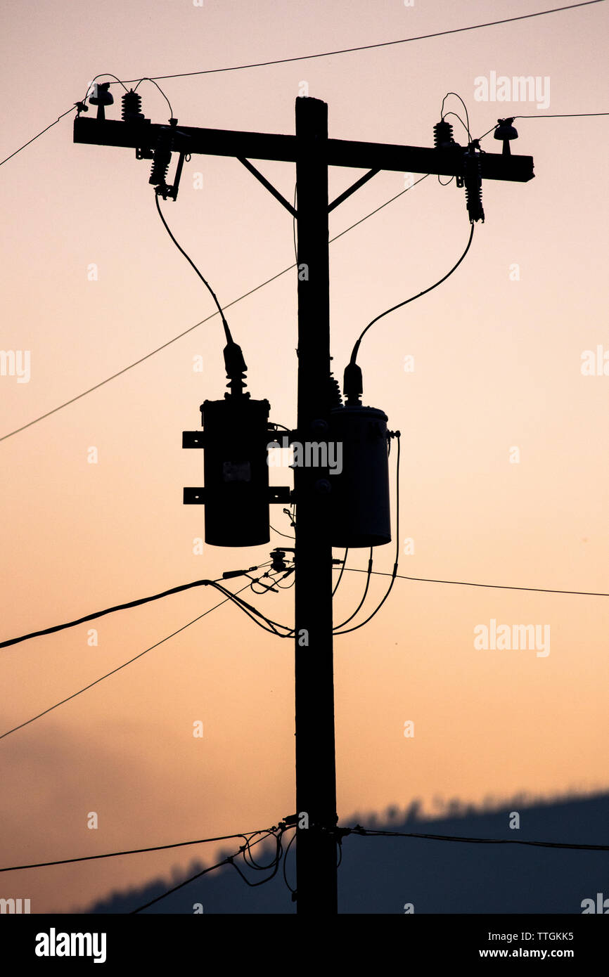 La silhouette d'un transformateur d'électricité sur une colonne d'alimentation au coucher du soleil. Banque D'Images