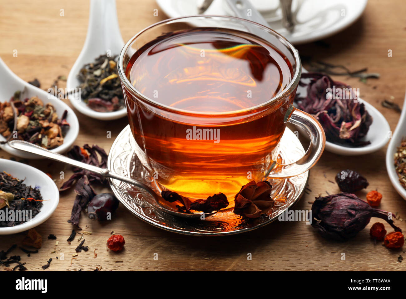 Concept de thé. Différents types de thé sec dans les cuillères. Tasse de thé en verre sur fond de bois Banque D'Images