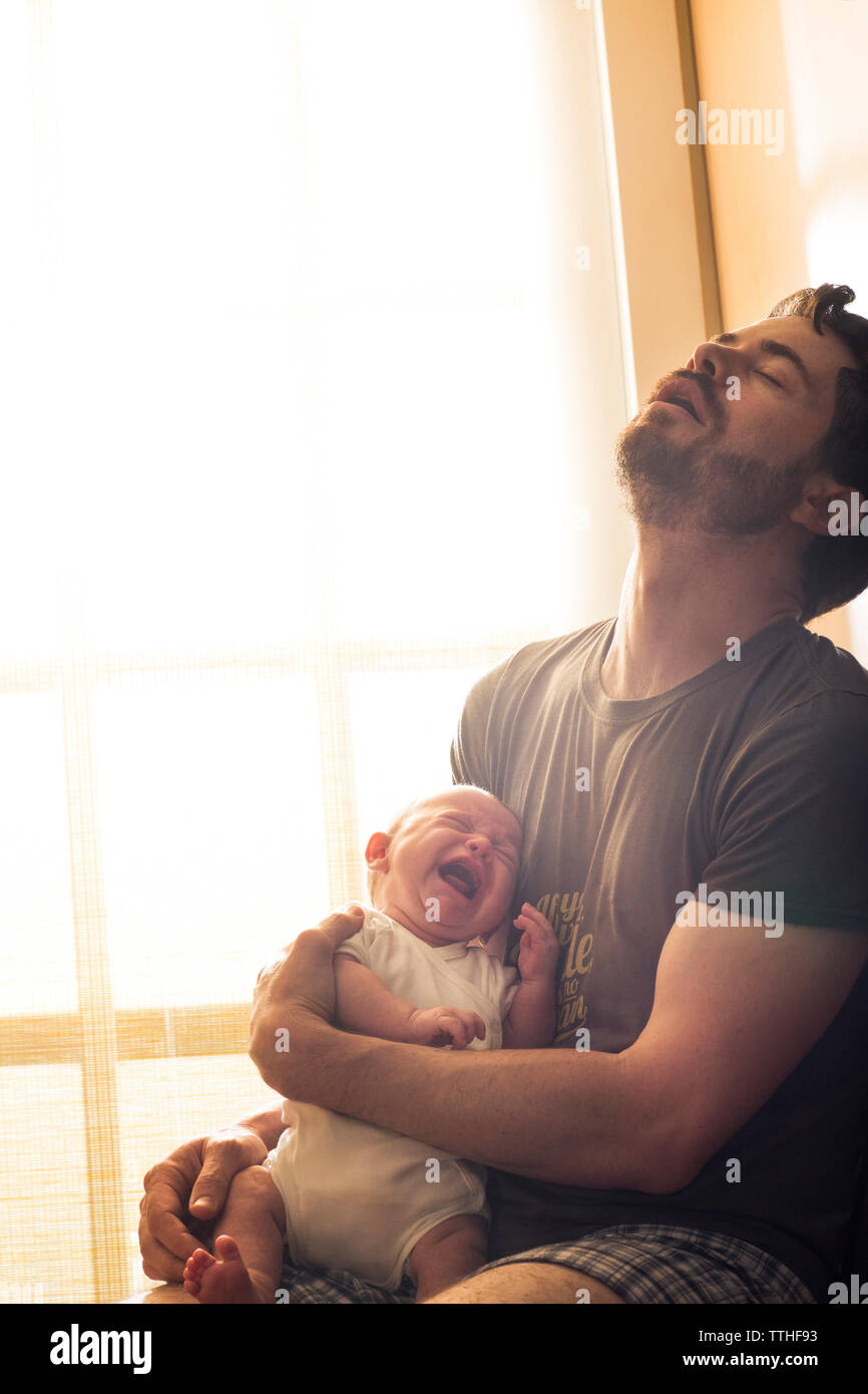 Père frustré holding crying baby fille contre fenêtre à Accueil Banque D'Images