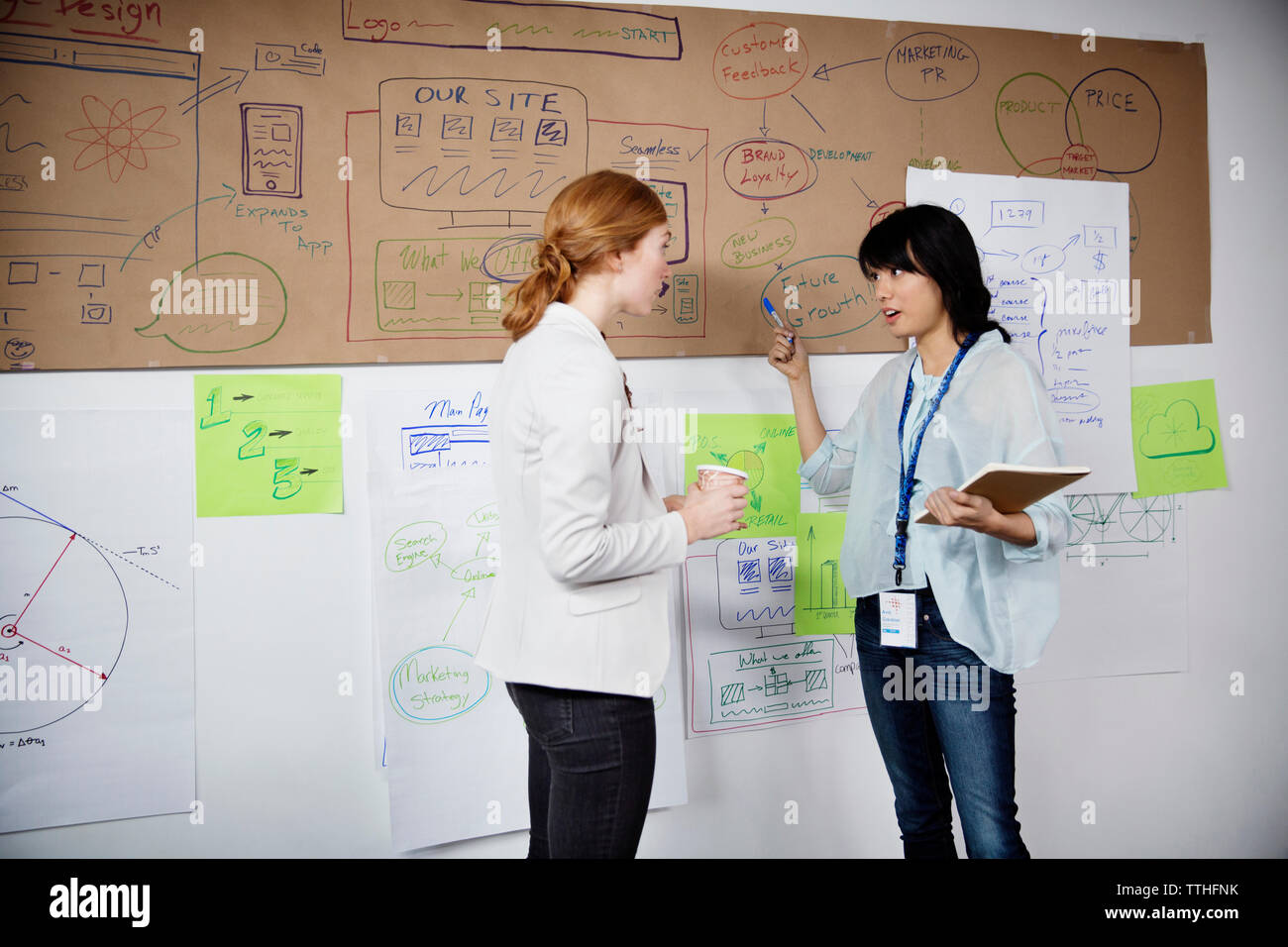 Plus de Businesswomen discussing charts alors que standing in office Banque D'Images