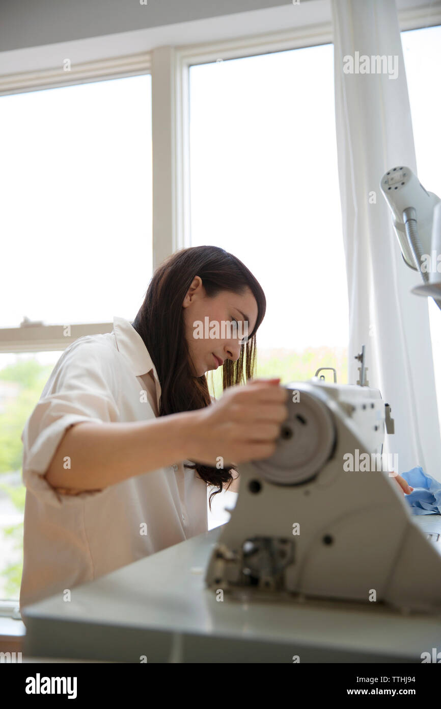 Vue latérale du designer de mode féminine travaillant sur machine à coudre dans studio Banque D'Images