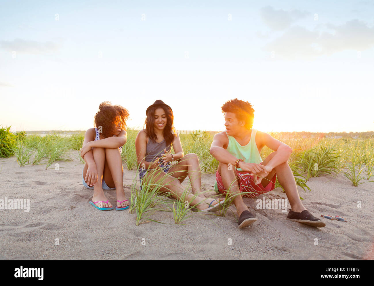 Heureux les amis de communiquer tout en restant assis sur la plage contre ciel sur sunny day Banque D'Images