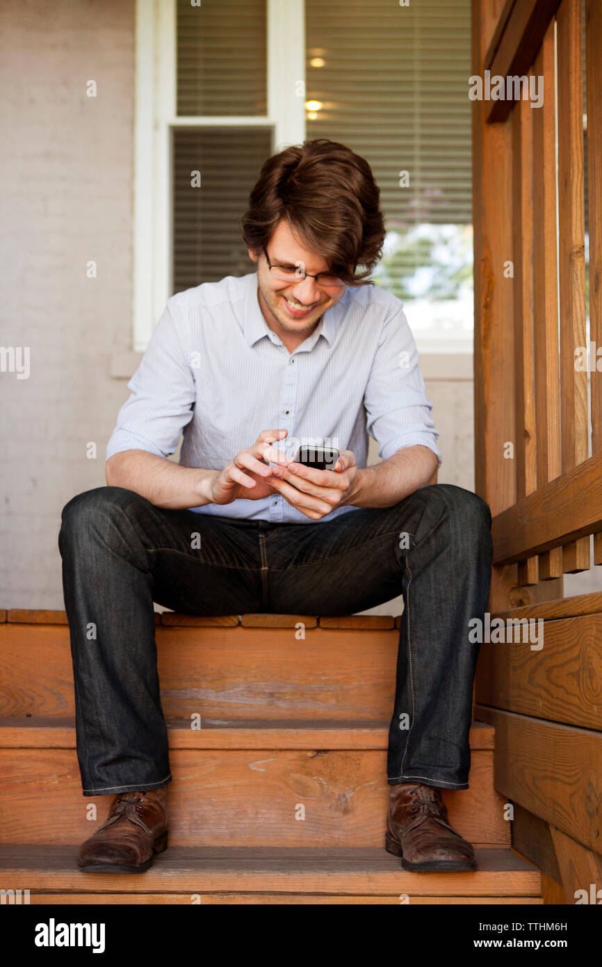Homme heureux avec phone while sitting on steps Banque D'Images