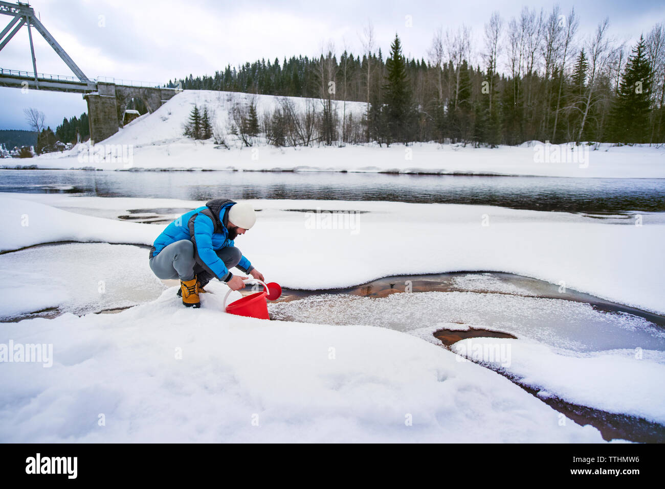 L'homme alors que la benne de remplissage accroupi sur une rivière couverte de neige Banque D'Images