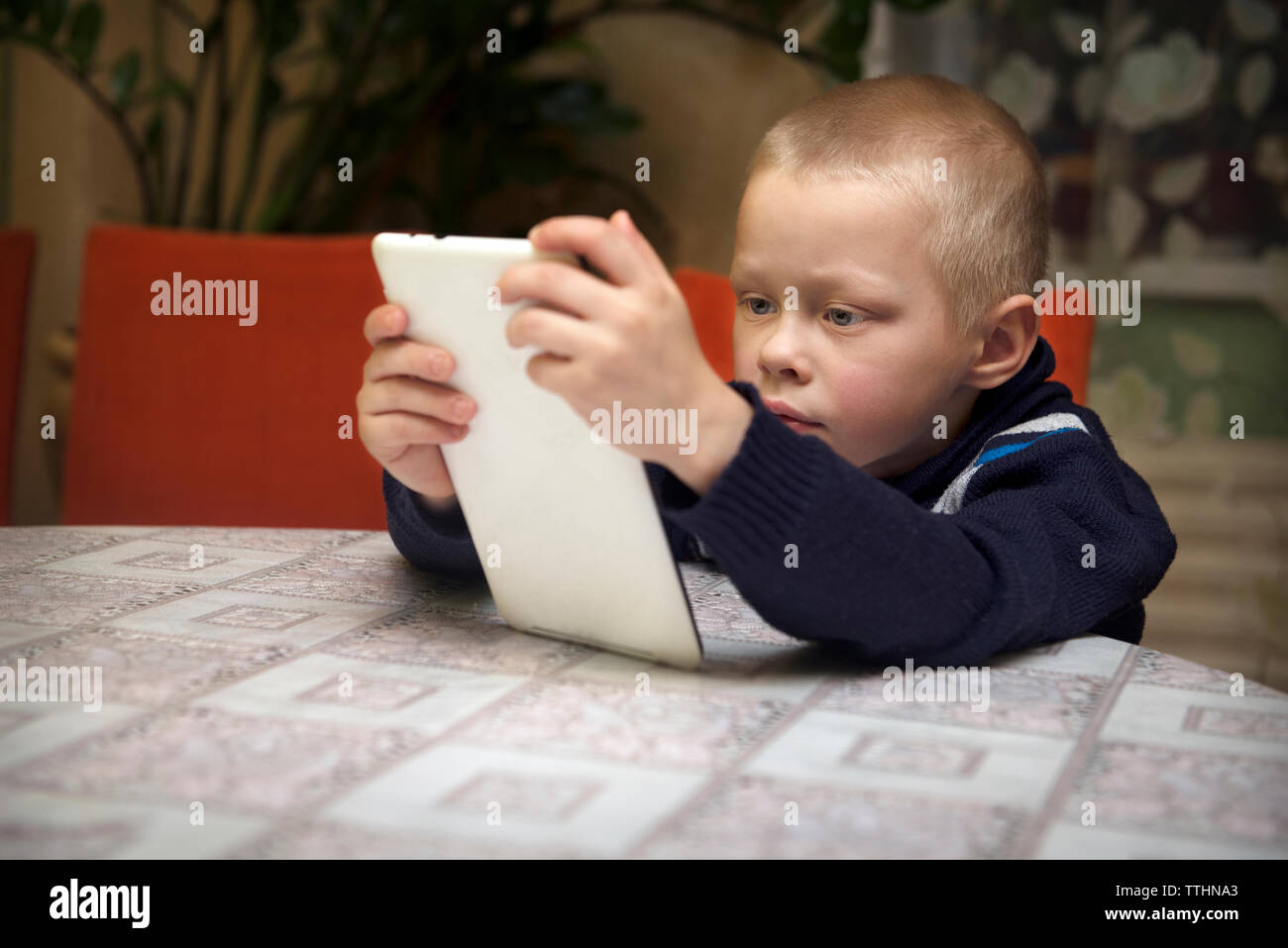 Boy using tablet computer while sitting at table Banque D'Images