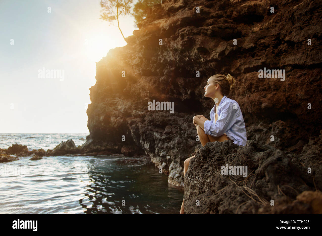 Thoughtful woman sitting on rock at beach Banque D'Images