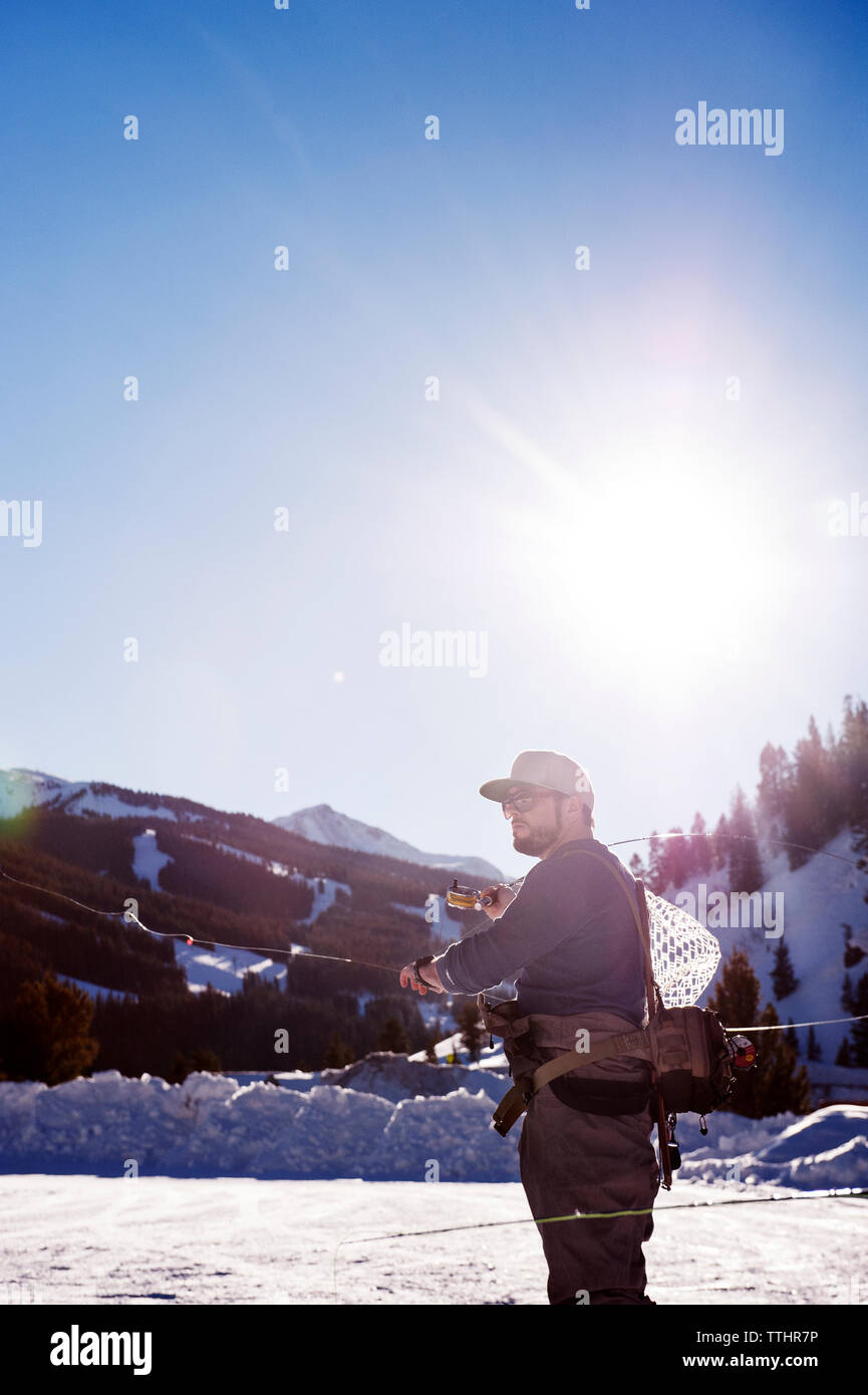 Fly fisherman casting canne à pêche en se tenant sur le champ neigeux contre ciel clair Banque D'Images