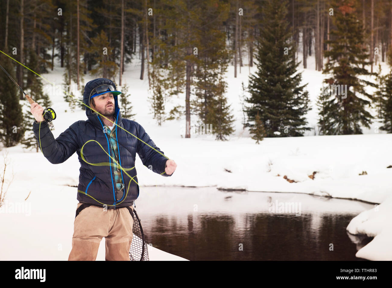 Fly fisherman casting canne à pêche en se tenant sur le champ neigeux Banque D'Images