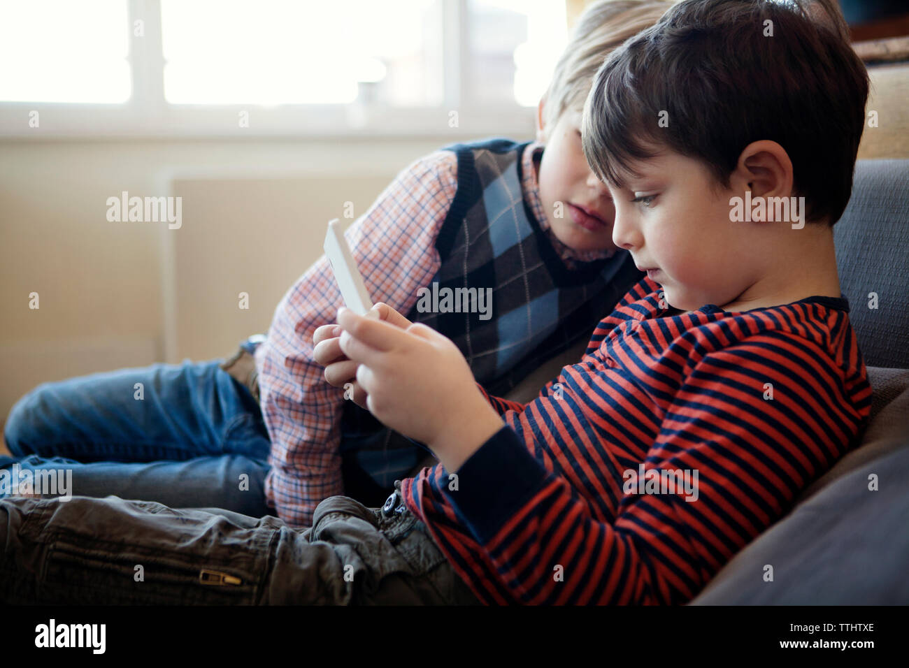 Siblings playing video game while sitting on sofa at home Banque D'Images