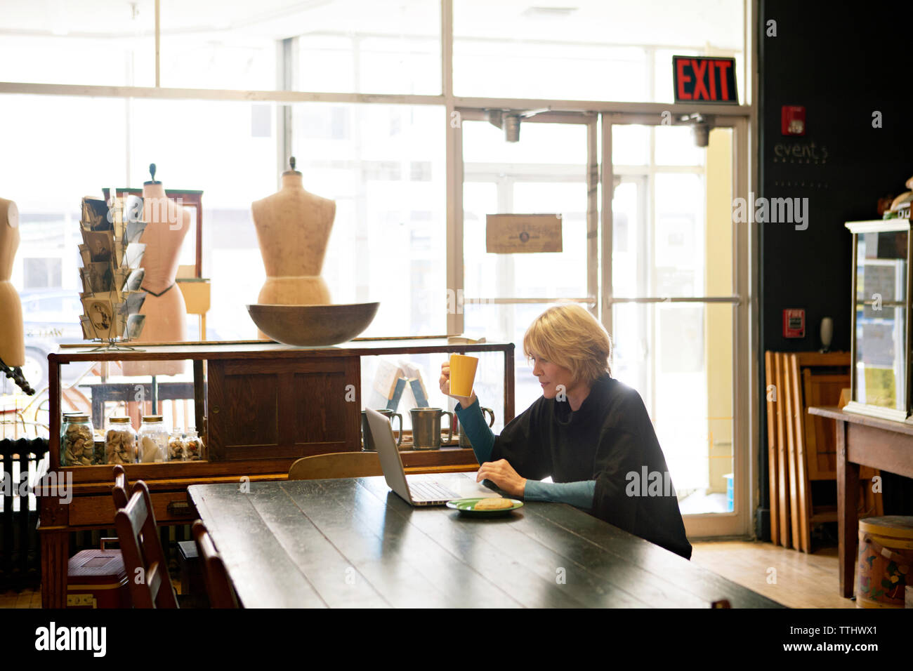 Woman using laptop while holding mug au magasin de vêtements Banque D'Images