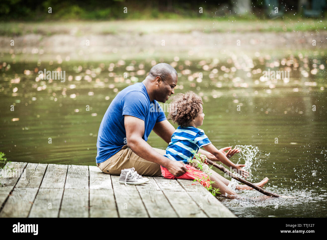 Famille heureuse aux projections d'eau tout en sitting on jetty at Lake Banque D'Images