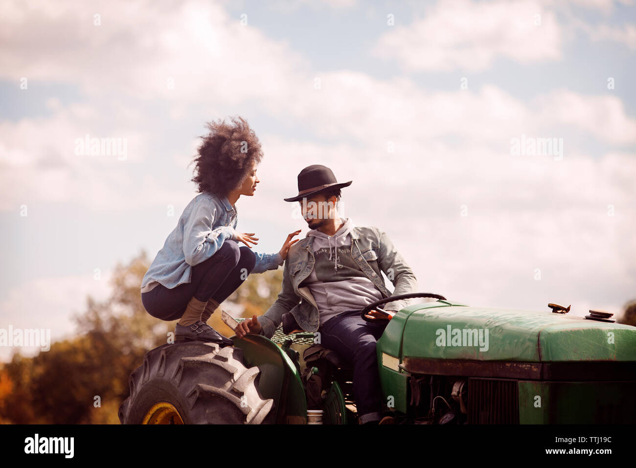 Couple sur le tracteur contre ciel nuageux Banque D'Images