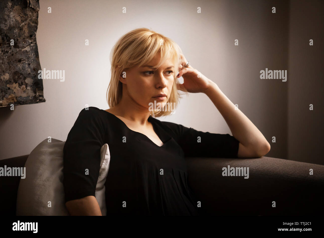 Thoughtful woman with hand in hair sitting on sofa at home Banque D'Images