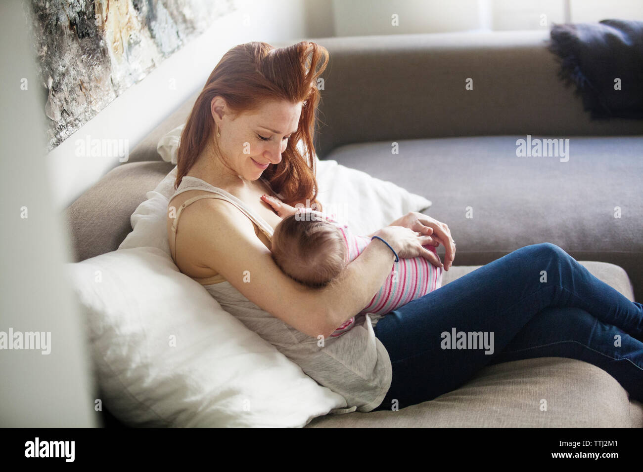 Heureux mère regardant bébé fille, assise sur un canapé Banque D'Images