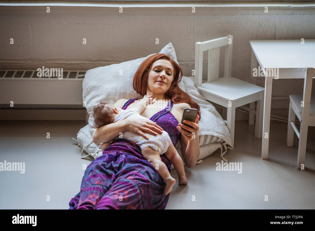 High angle view of mother with baby girl using mobile phone while lying on floor at home Banque D'Images