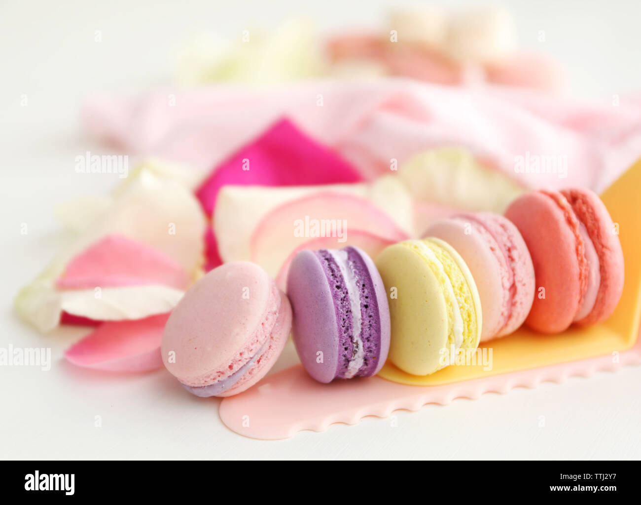 Des macarons et des pétales de rose sur fond blanc Banque D'Images