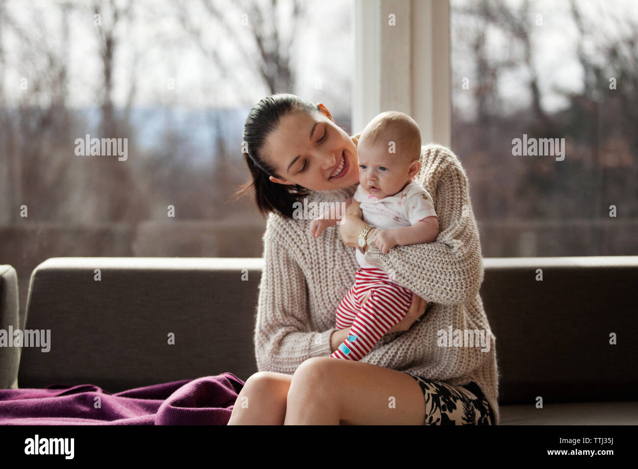 Happy woman holding baby girl while sitting on sofa at home Banque D'Images