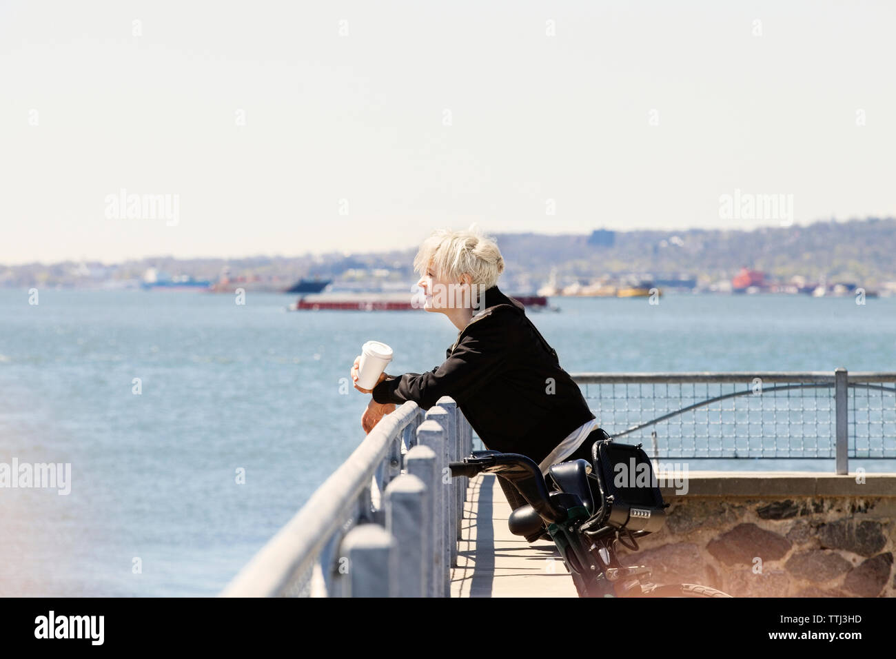 Woman leaning on railing au point d'observation par river contre ciel clair Banque D'Images