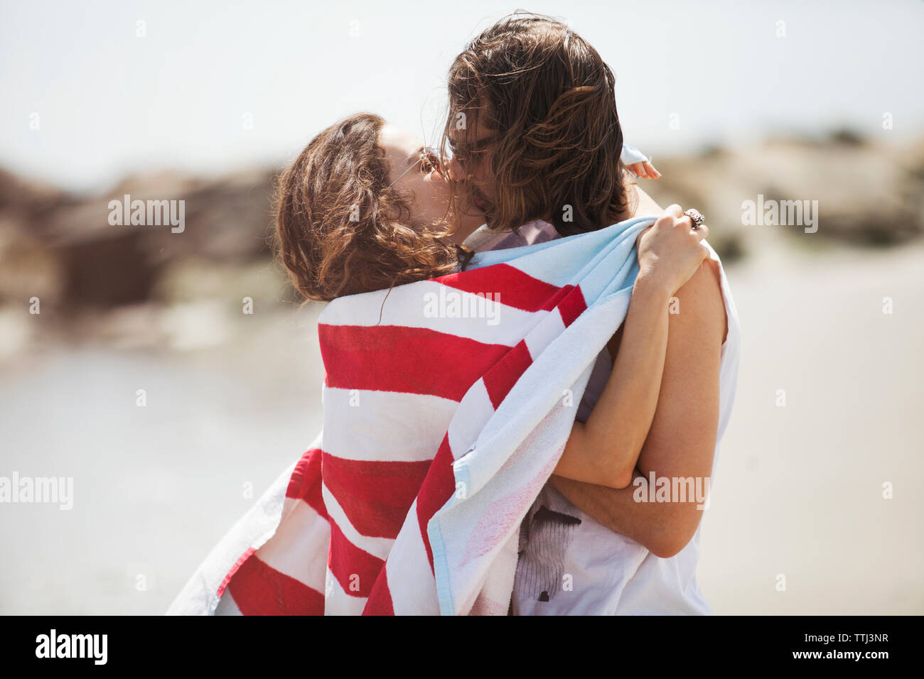 Vue de côté de femme enveloppée dans tout contrat cadre kissing man on beach Banque D'Images