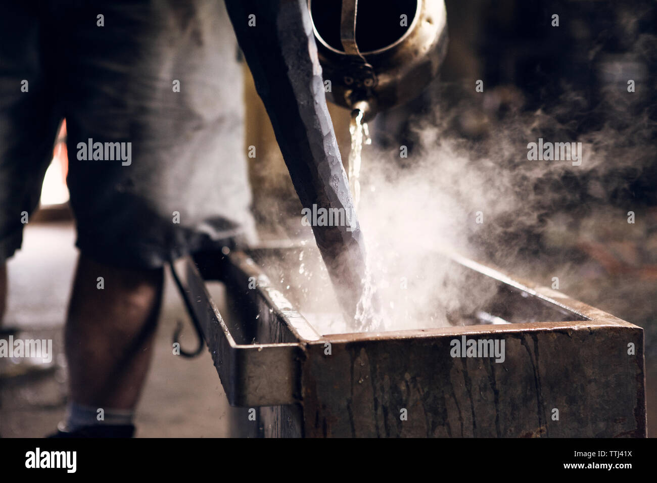 Au milieu du forgeron verser de l'eau sur hot rod en atelier Banque D'Images