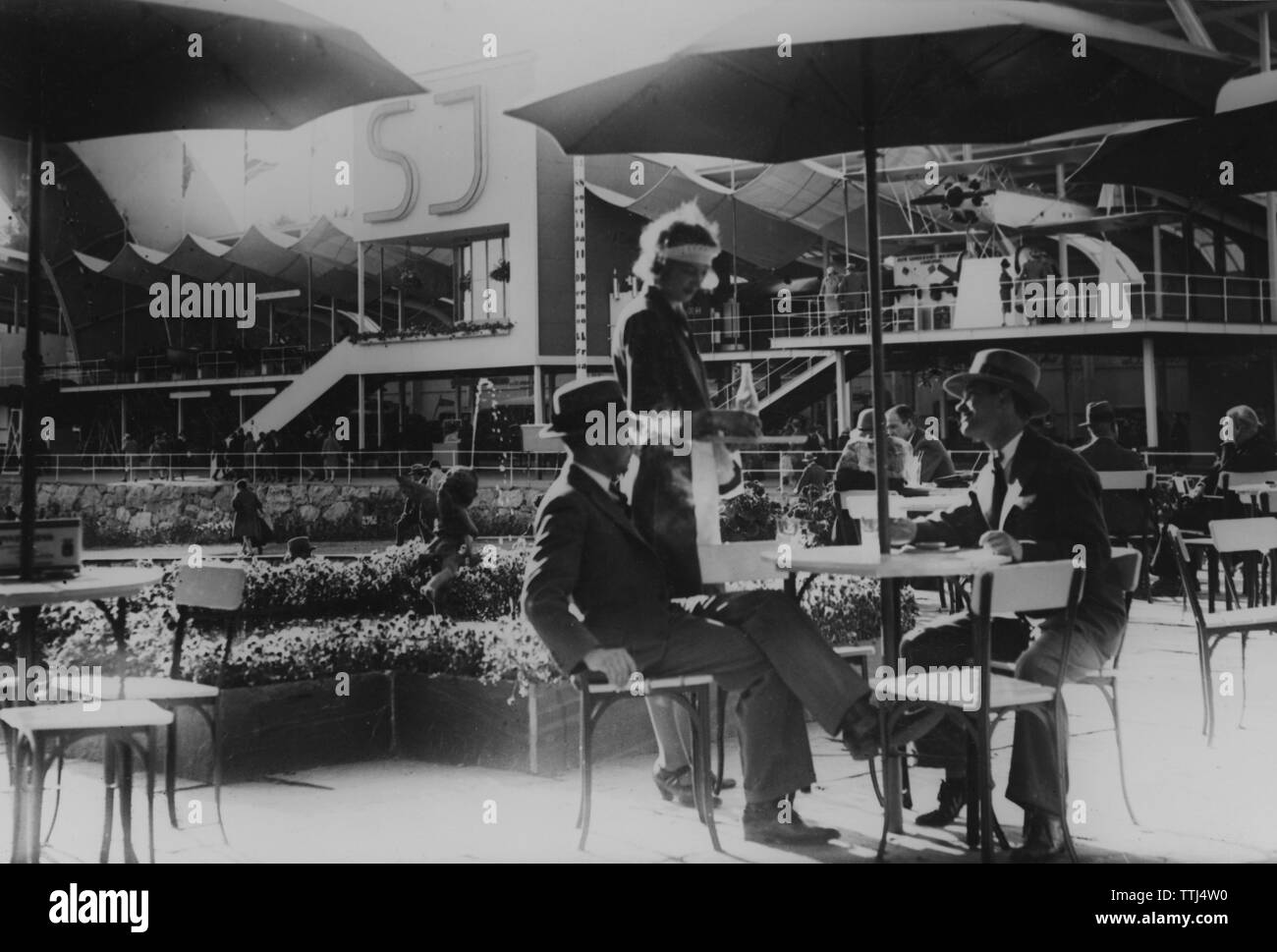 1930 café en plein air. Deux hommes sont servies des boissons à la table par une serveuse au motif de l'exposition de Stockholm de 1930. Banque D'Images
