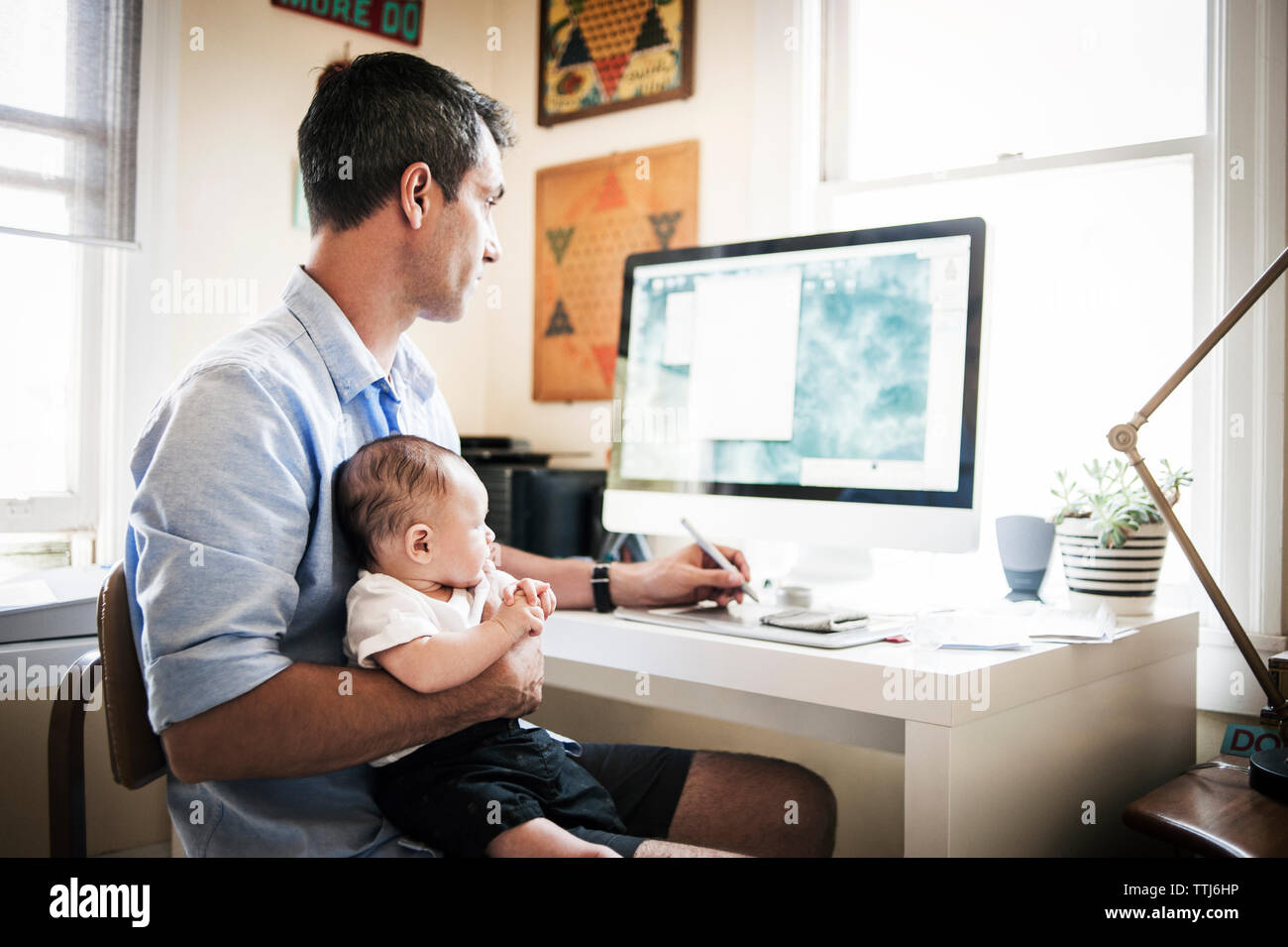 Man carrying baby boy tout en travaillant sur l'ordinateur de bureau à la maison Banque D'Images