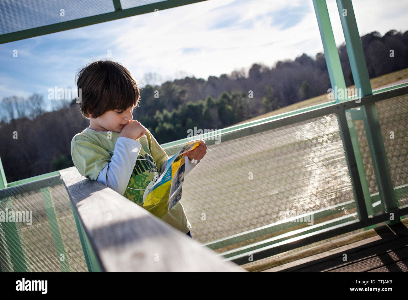 Boy reading brochure debout by railing Banque D'Images