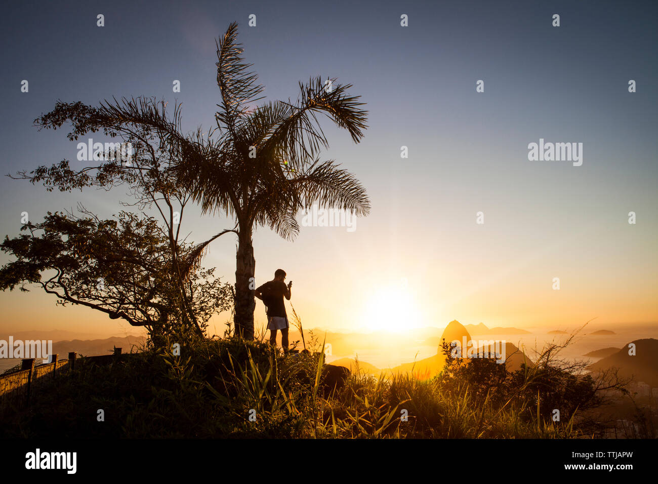 L'homme à l'aide de téléphone mobile en position debout contre le mont Sugarloaf pendant le coucher du soleil Banque D'Images