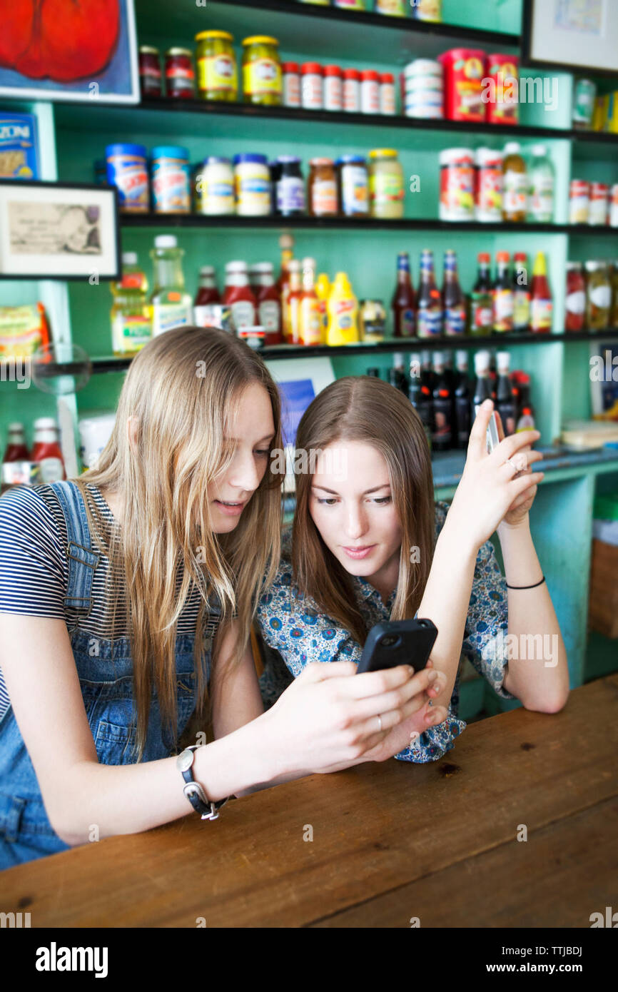 Friends looking at mobile phone while sitting in store Banque D'Images