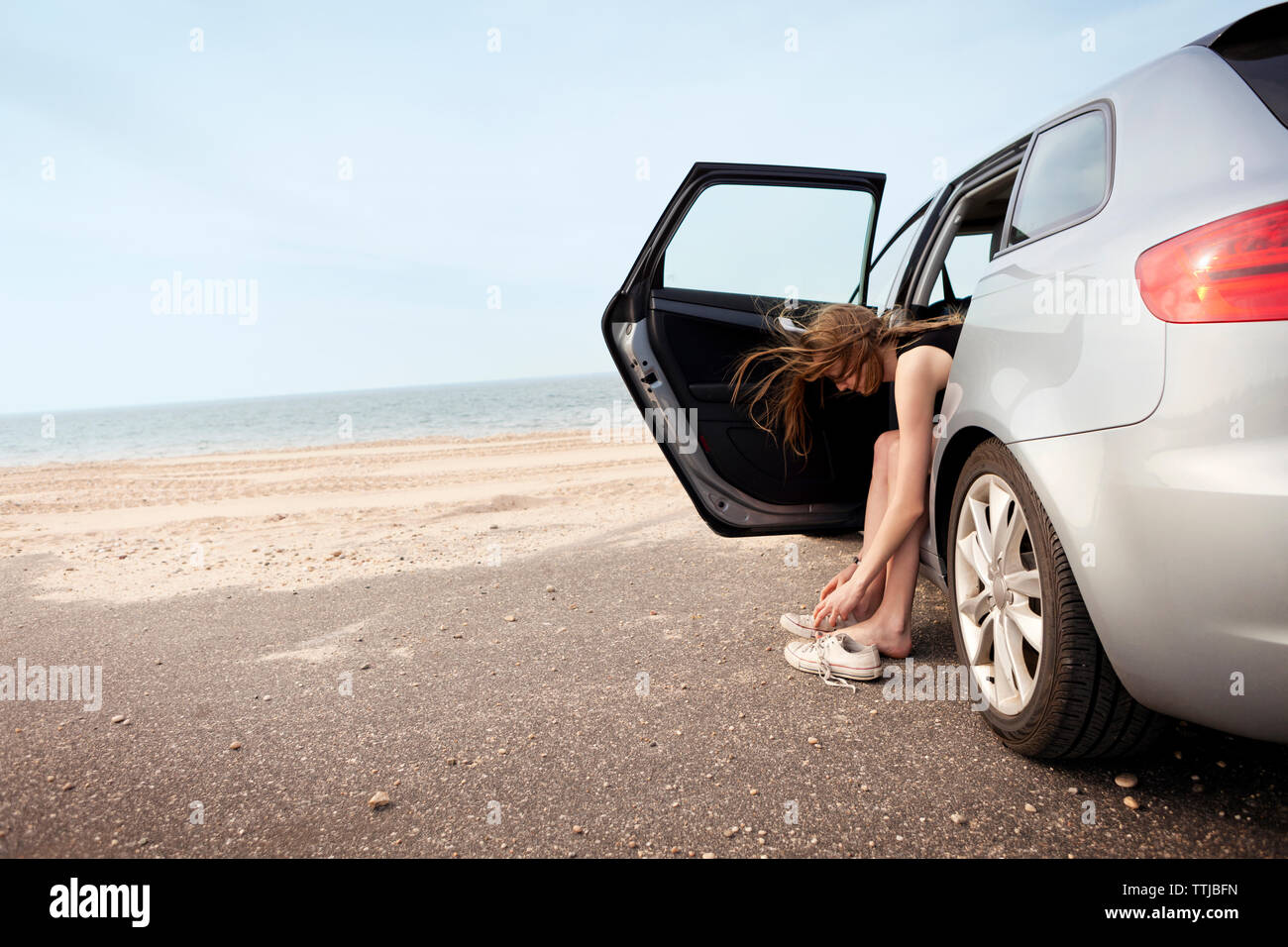 Femme portant des chaussures tout en restant assis dans la voiture à la plage Banque D'Images
