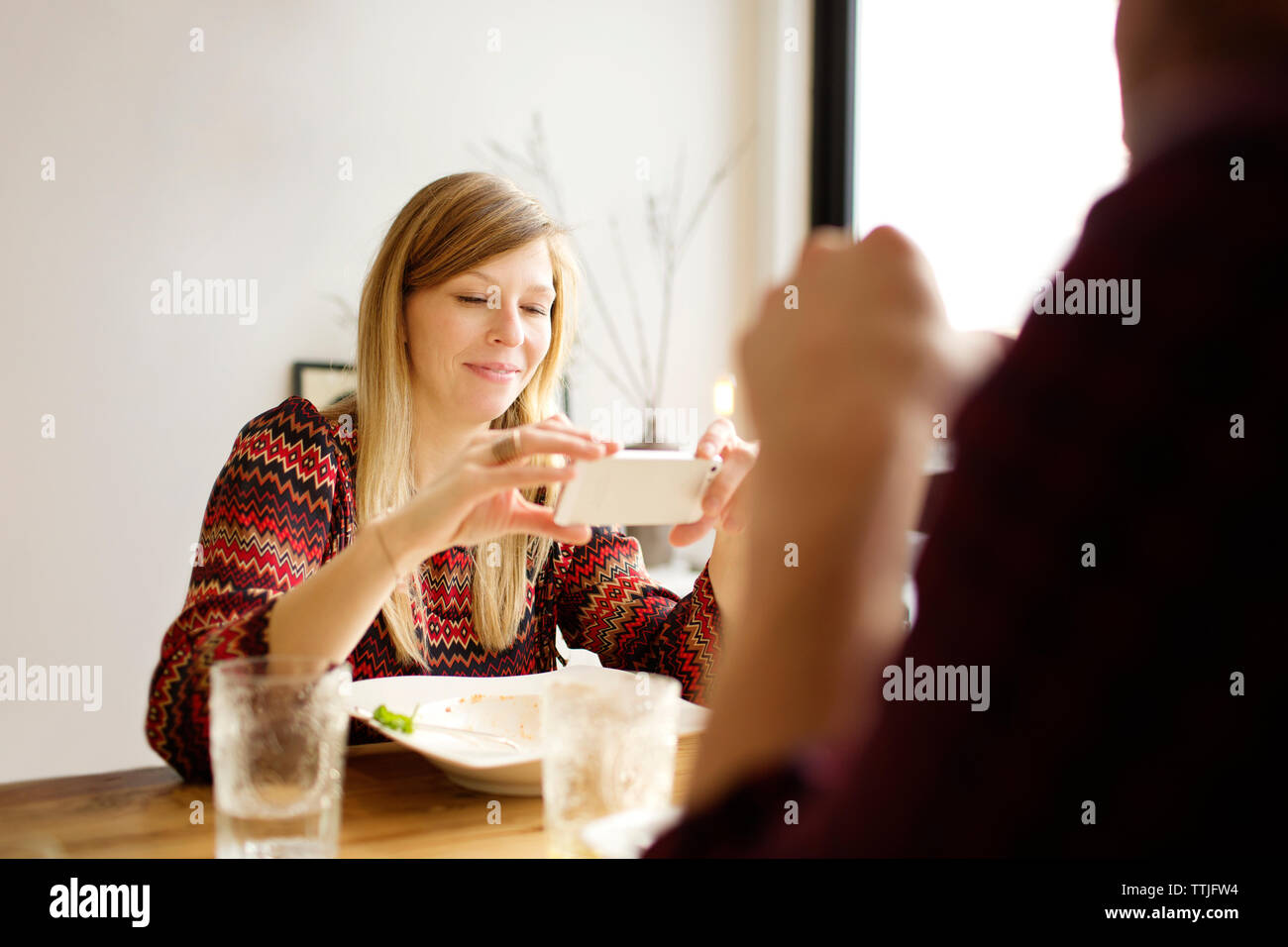 Woman using mobile phone while sitting par l'homme à table à manger dans la maison Banque D'Images