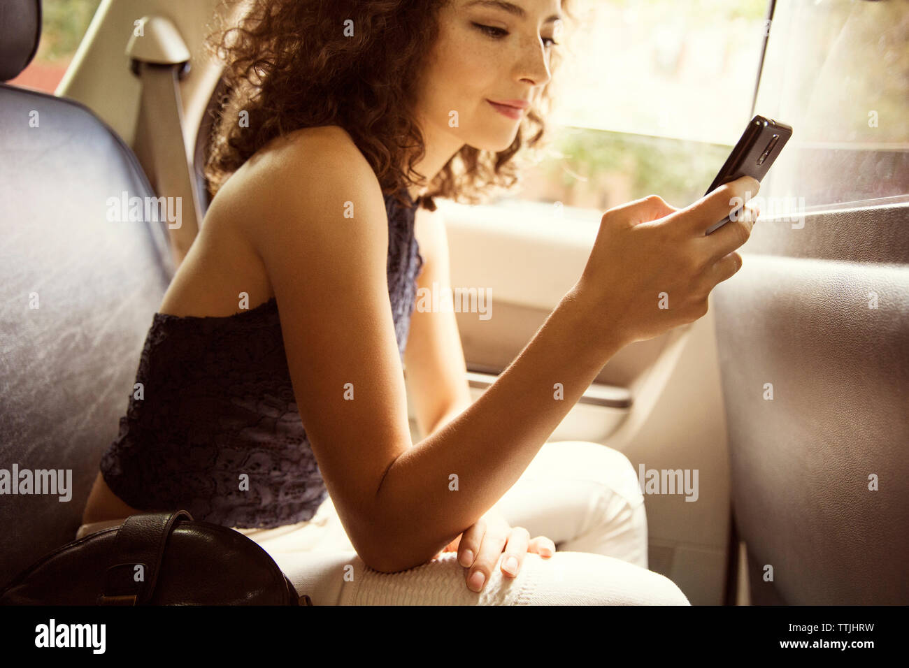 Vue latérale de la femme à l'aide de smart phone alors qu'en voyageant en voiture Banque D'Images