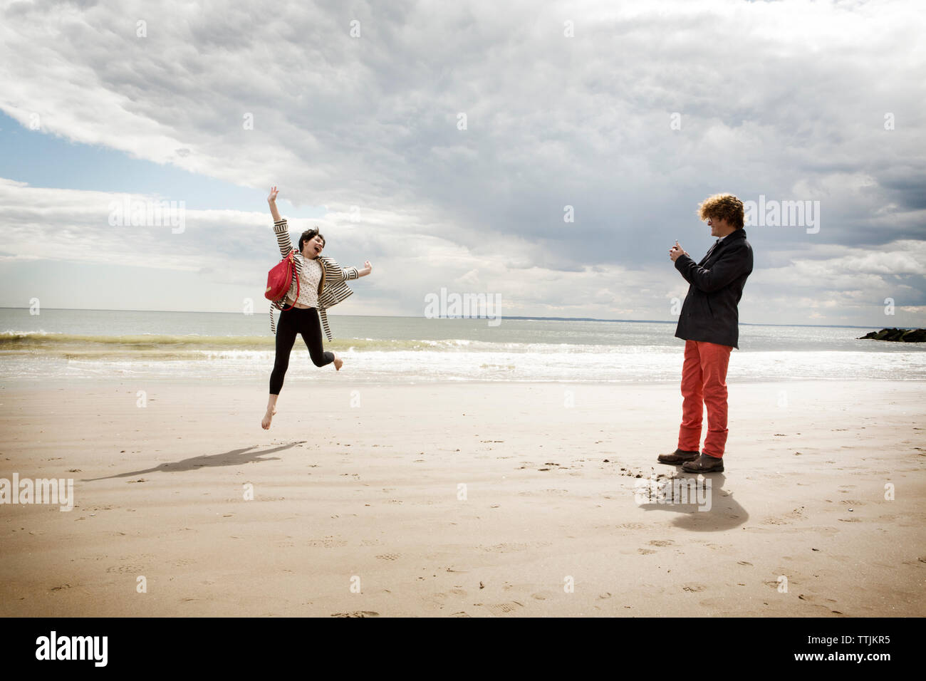 Man photographing jumping femme en se tenant sur le sand at beach Banque D'Images