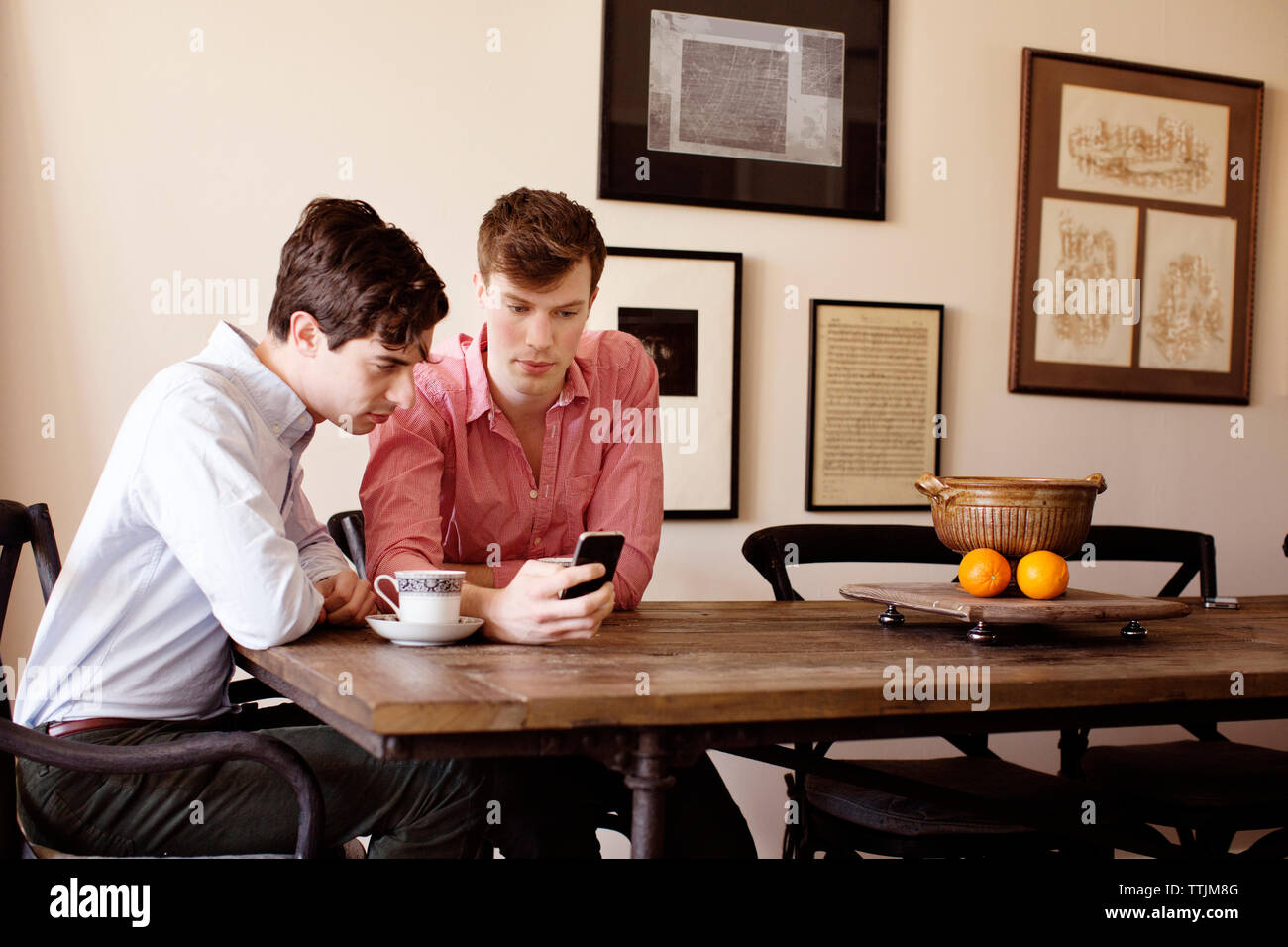 Gay-men looking at smart phone en étant assis par table Banque D'Images