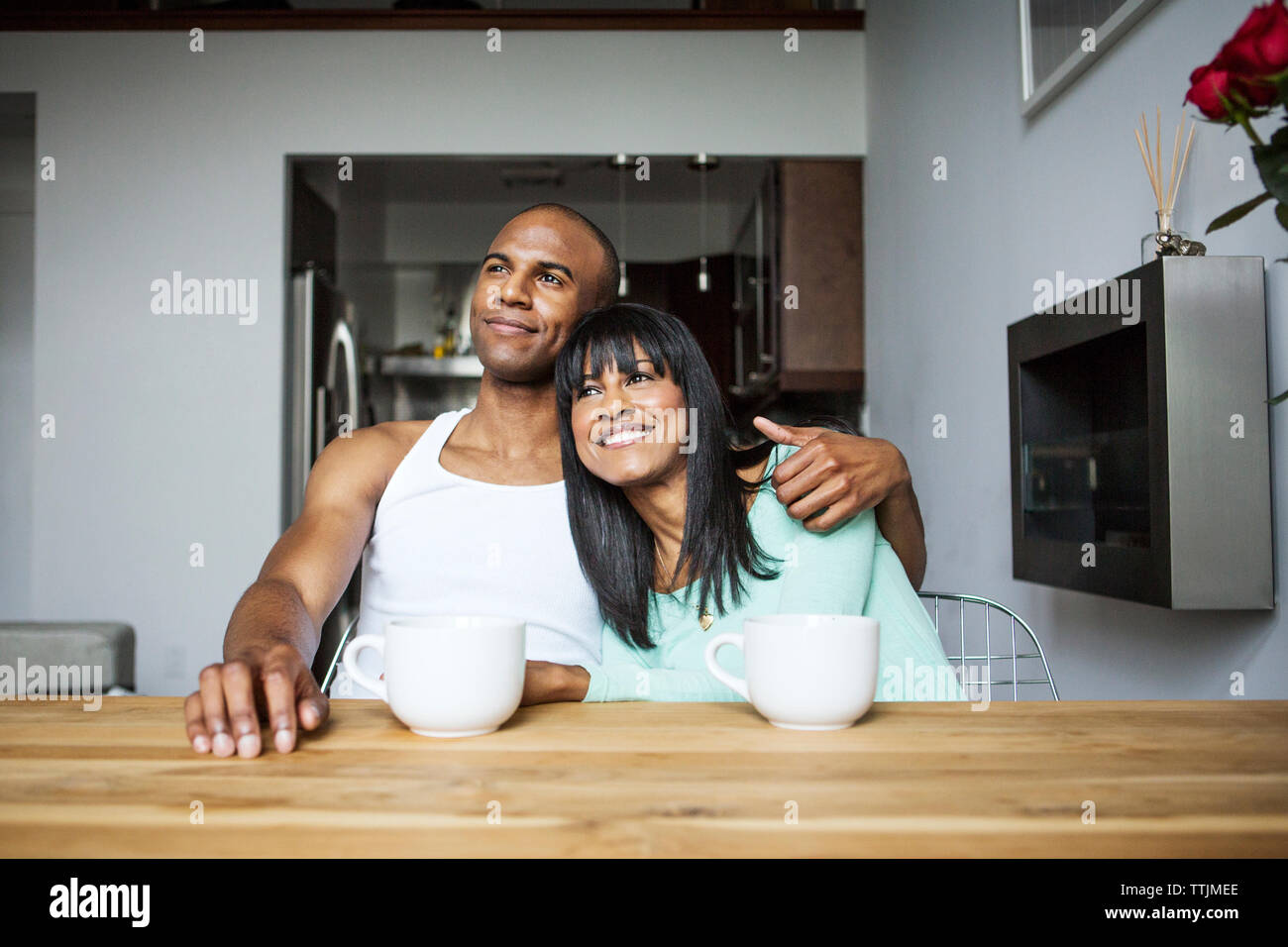 Smiling couple looking away while sitting by table à la maison Banque D'Images Smiling couple looking away while sitting by table à la maison Banque D'Images