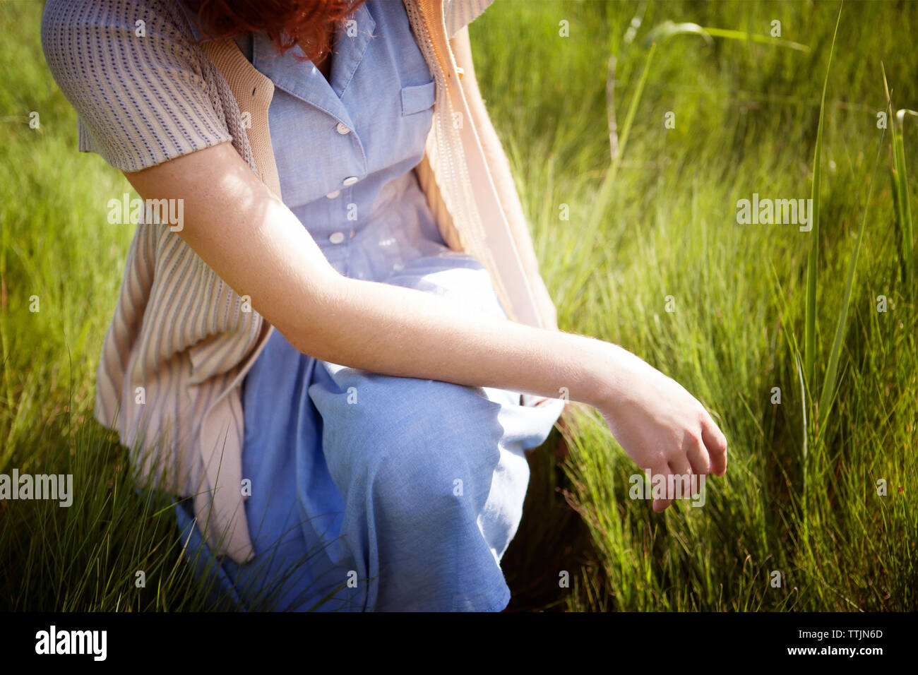 Midsection of woman crouching on grassy field Banque D'Images