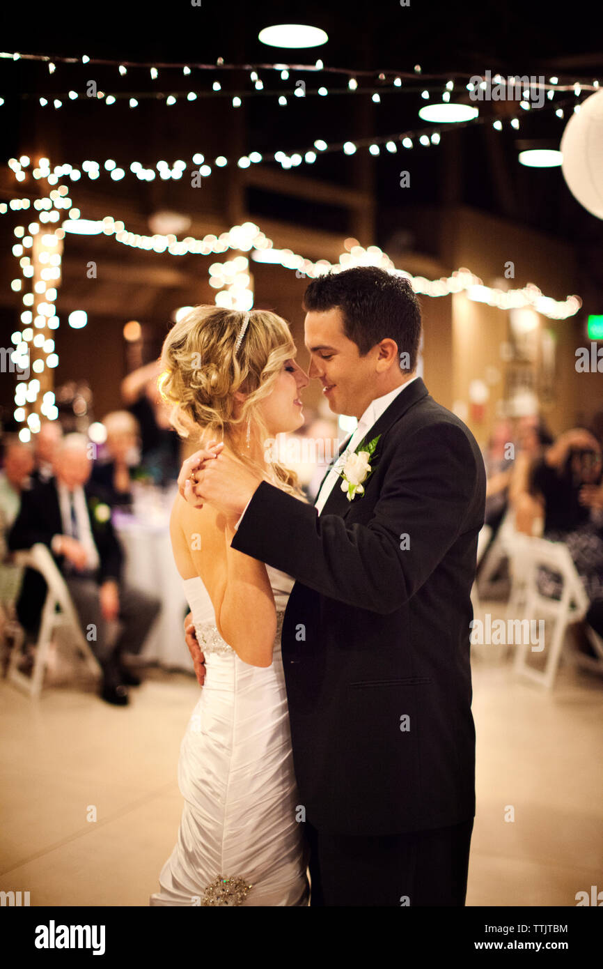 Jeunes mariés dansant dans la salle illuminée pendant wedding Banque D'Images