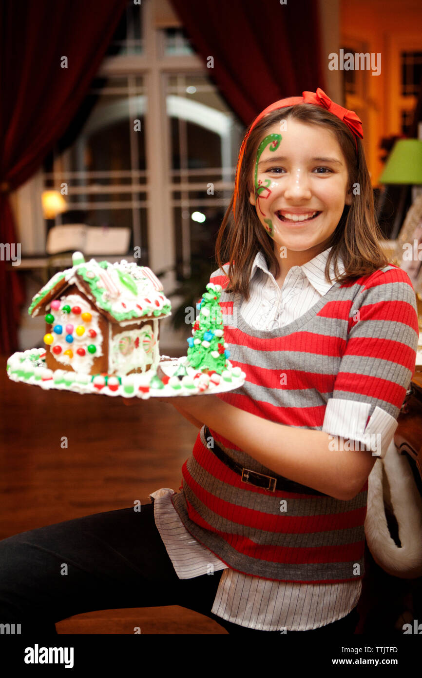 Portrait of smiling girl with face paint holding gingerbread house Banque D'Images