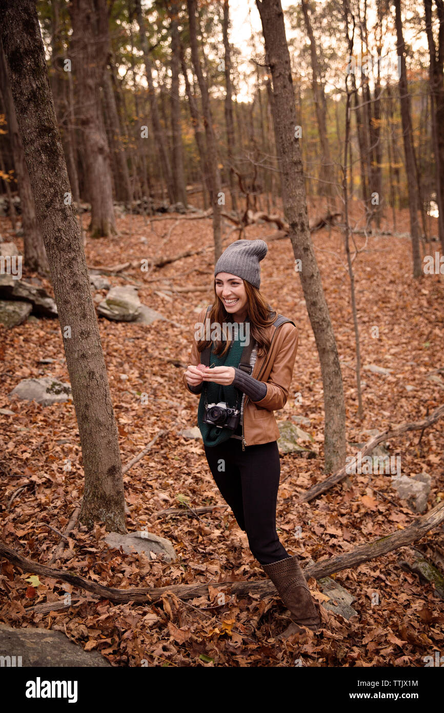 Femme souriante avec l'appareil photo au milieu d'arbres en forêt permanent pendant l'hiver Banque D'Images
