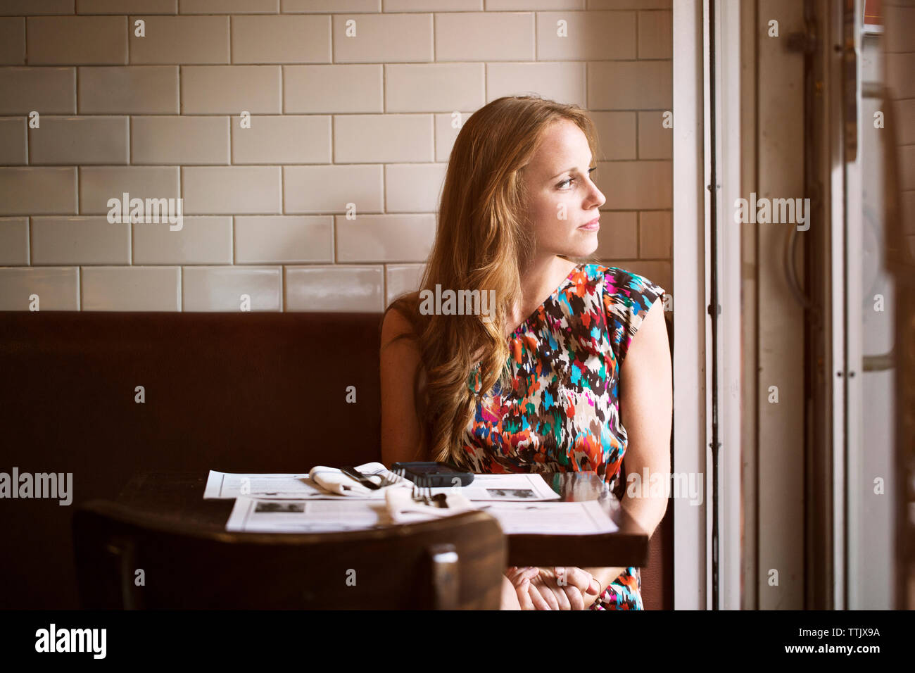 Thoughtful woman looking away while sitting in restaurant Banque D'Images