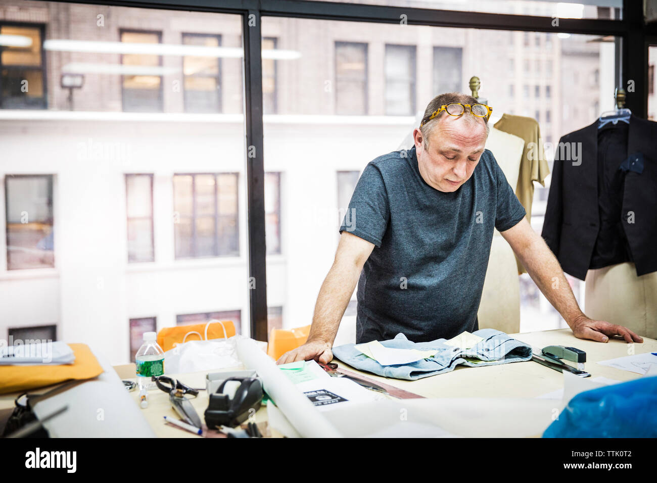 Créateur de mode sérieux à la recherche de jeans sur table contre la fenêtre en verre au design studio Banque D'Images