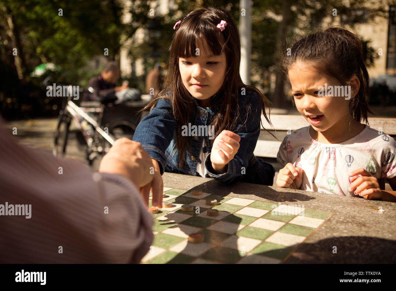 Sœurs jouer aux dames jeu avec grand-père alors qu'il était assis à table en park Banque D'Images