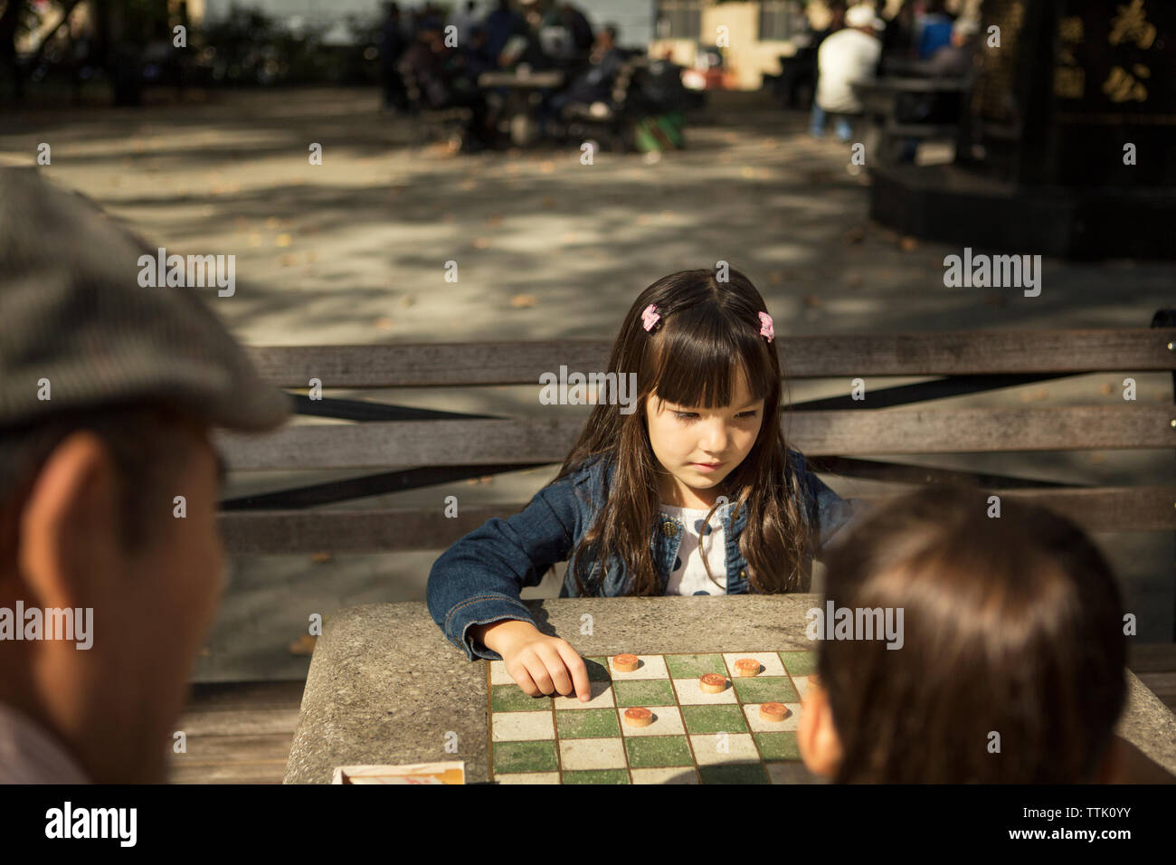 Jeune fille à la recherche vers le bas tout en jouant le jeu de dames avec sœur dans park Banque D'Images