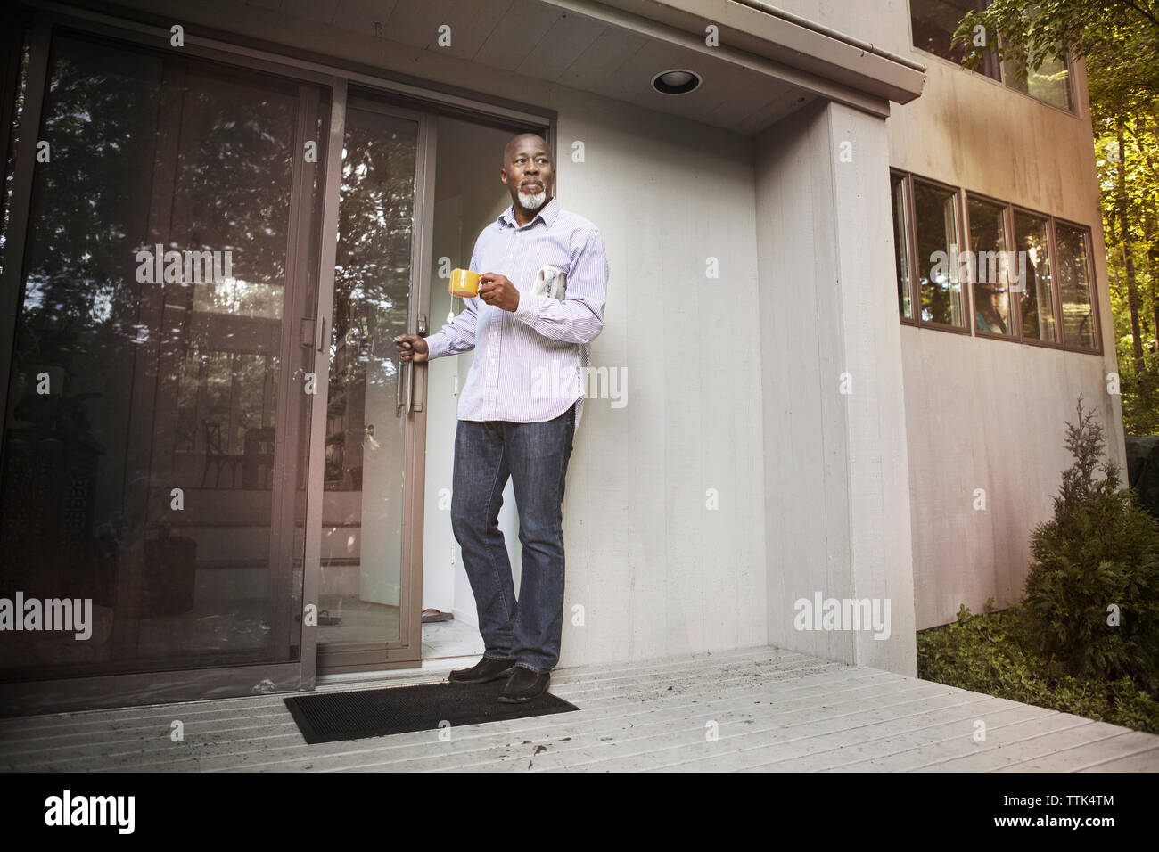 Senior man holding Coffee cup alors qu'il se tenait à l'entrée de la maison Banque D'Images