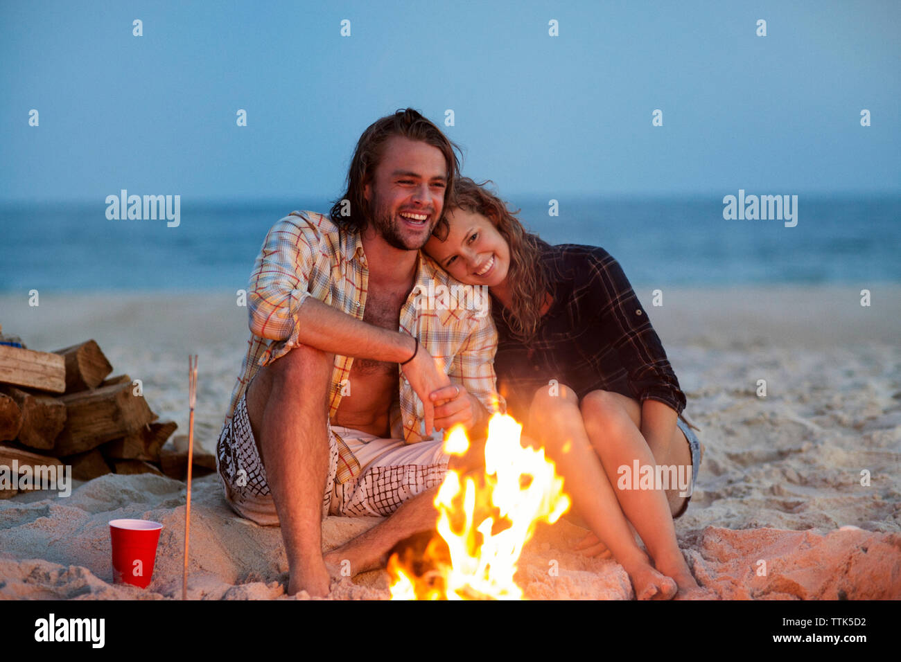 Cheerful couple sitting on sand par bonfire at beach Banque D'Images