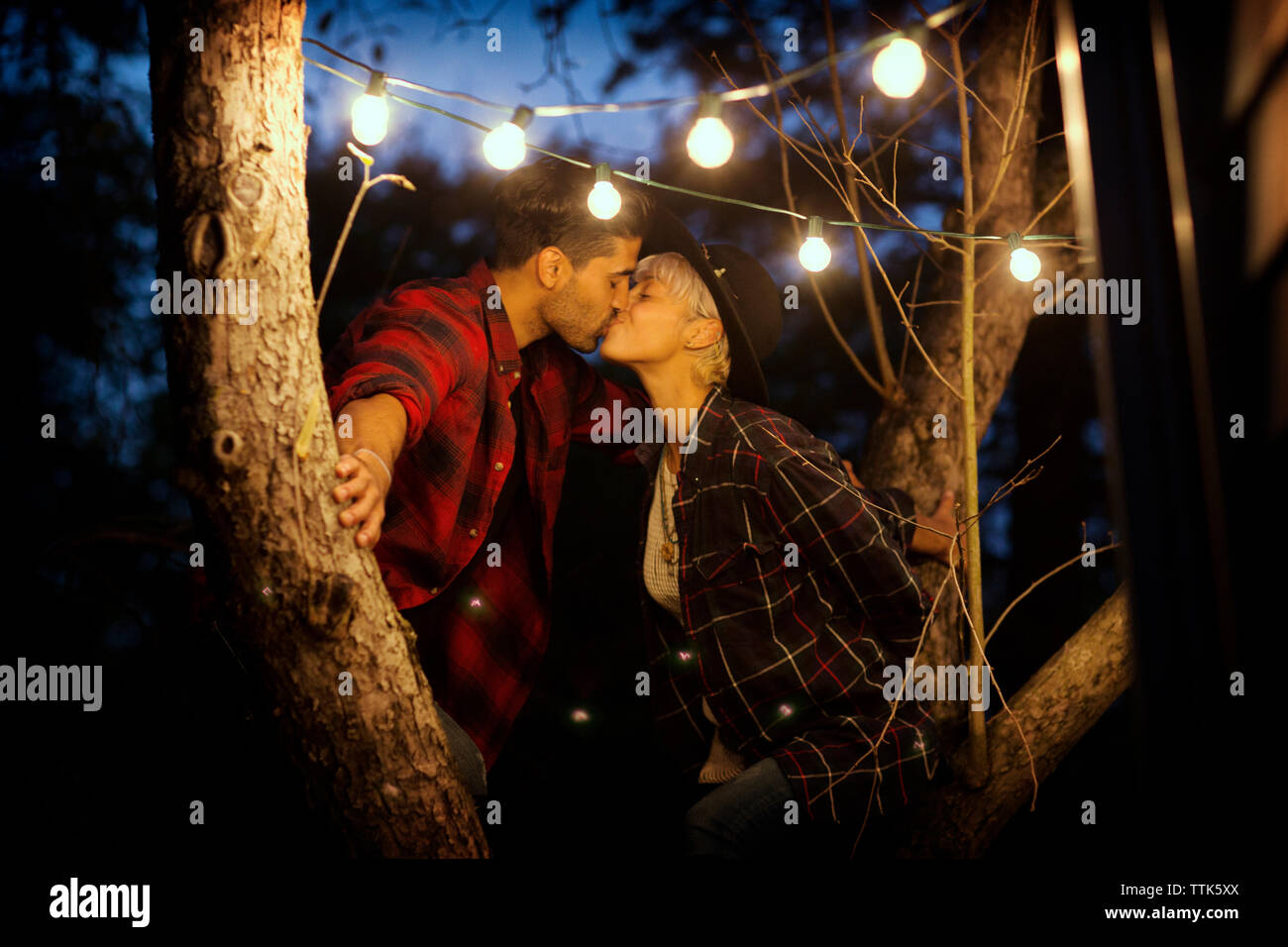 Affectionate couple kissing while sitting on tree Banque D'Images